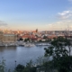 A panoramic view of a city featuring the river, historic buildings, and a clear sky.